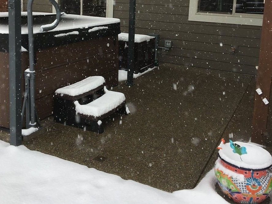 Covered patio beside a hot tub with a clear floor while snow lies around it